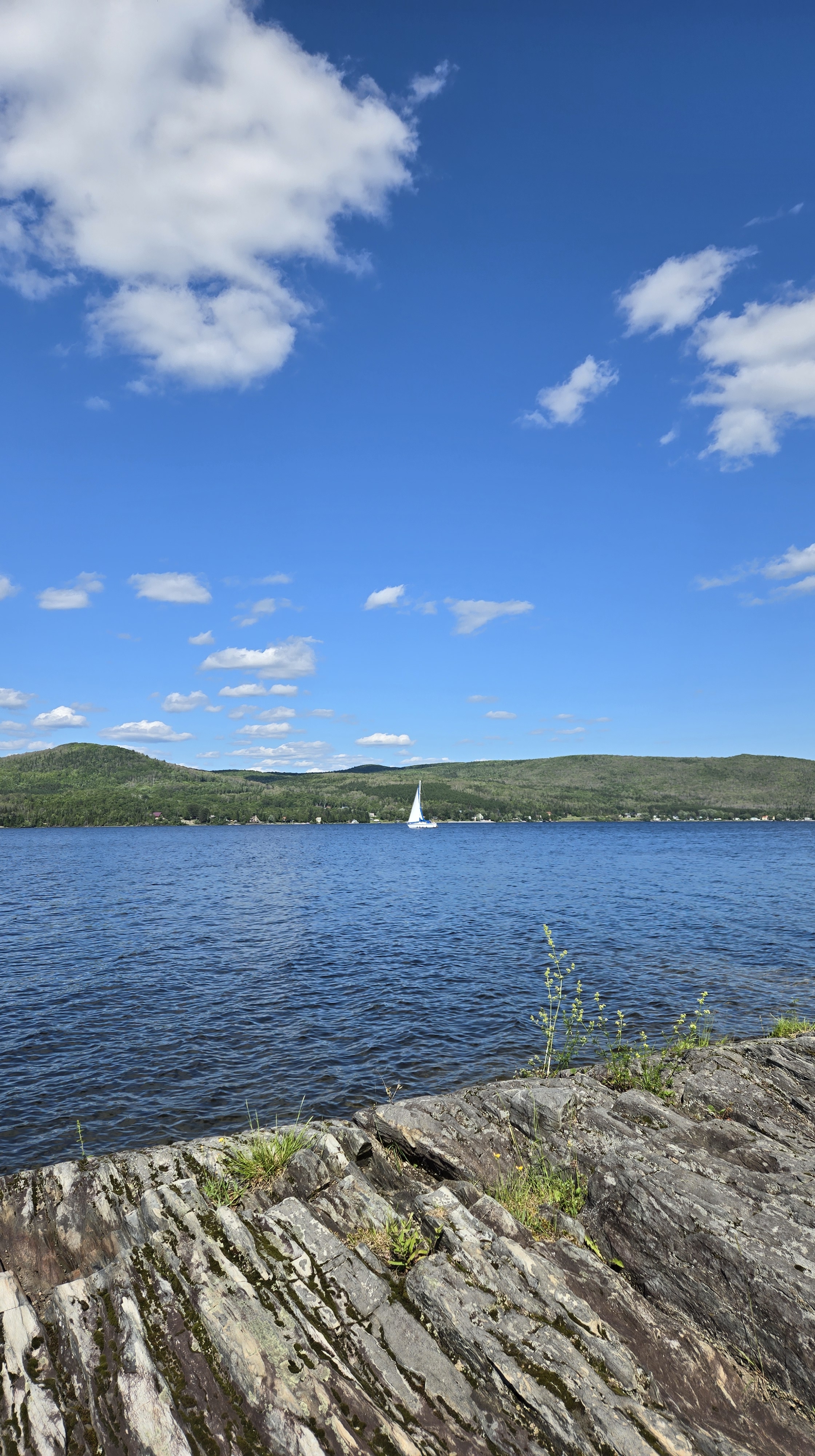 Pointe rocheuse qui s'avance dans le lac Témiscouata avec un voilier qui navigue au loin