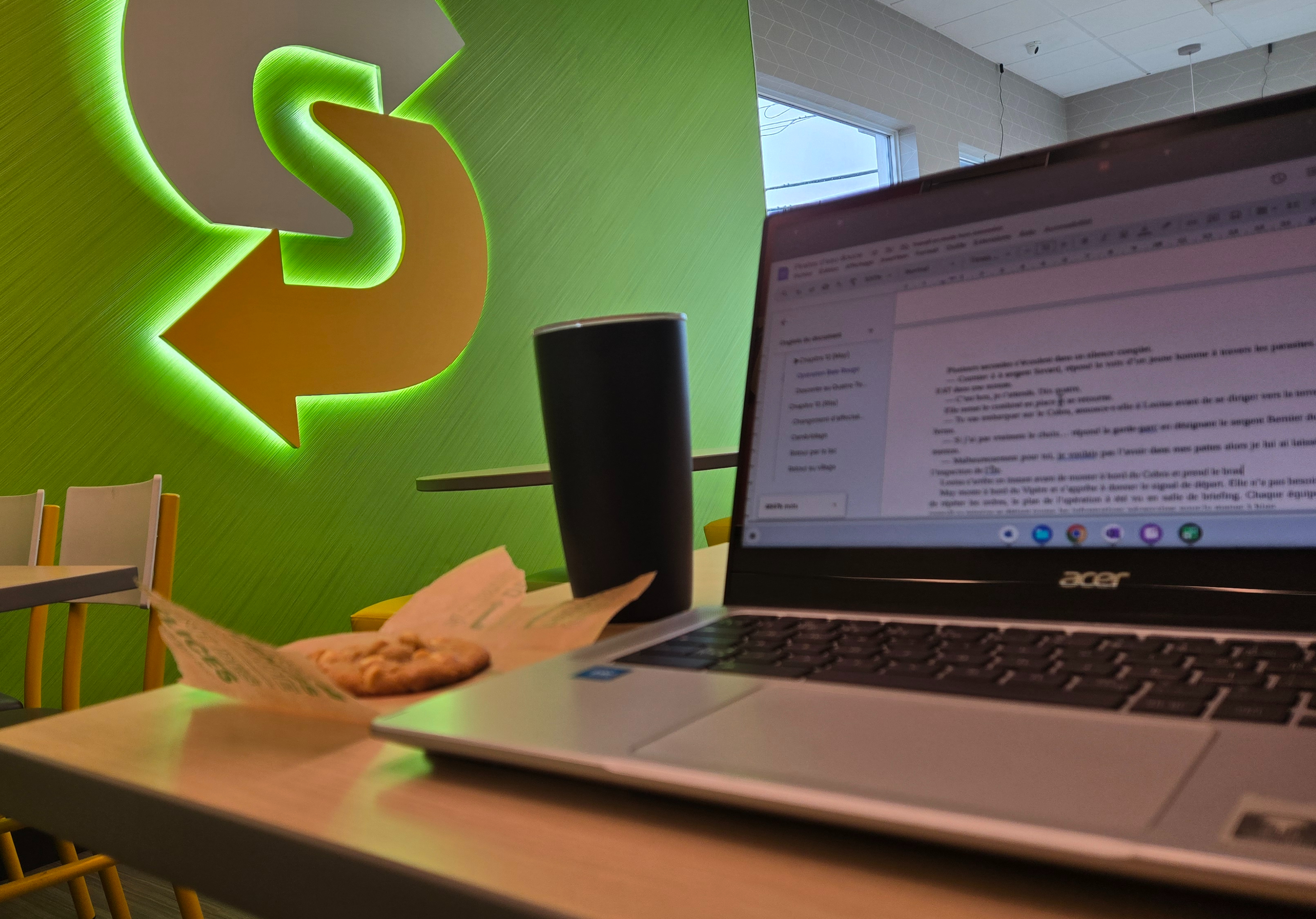 Ordinateur portable avec une tasse thermale et un biscuit macadam dans le décor vibrant d'un restaurant Subway