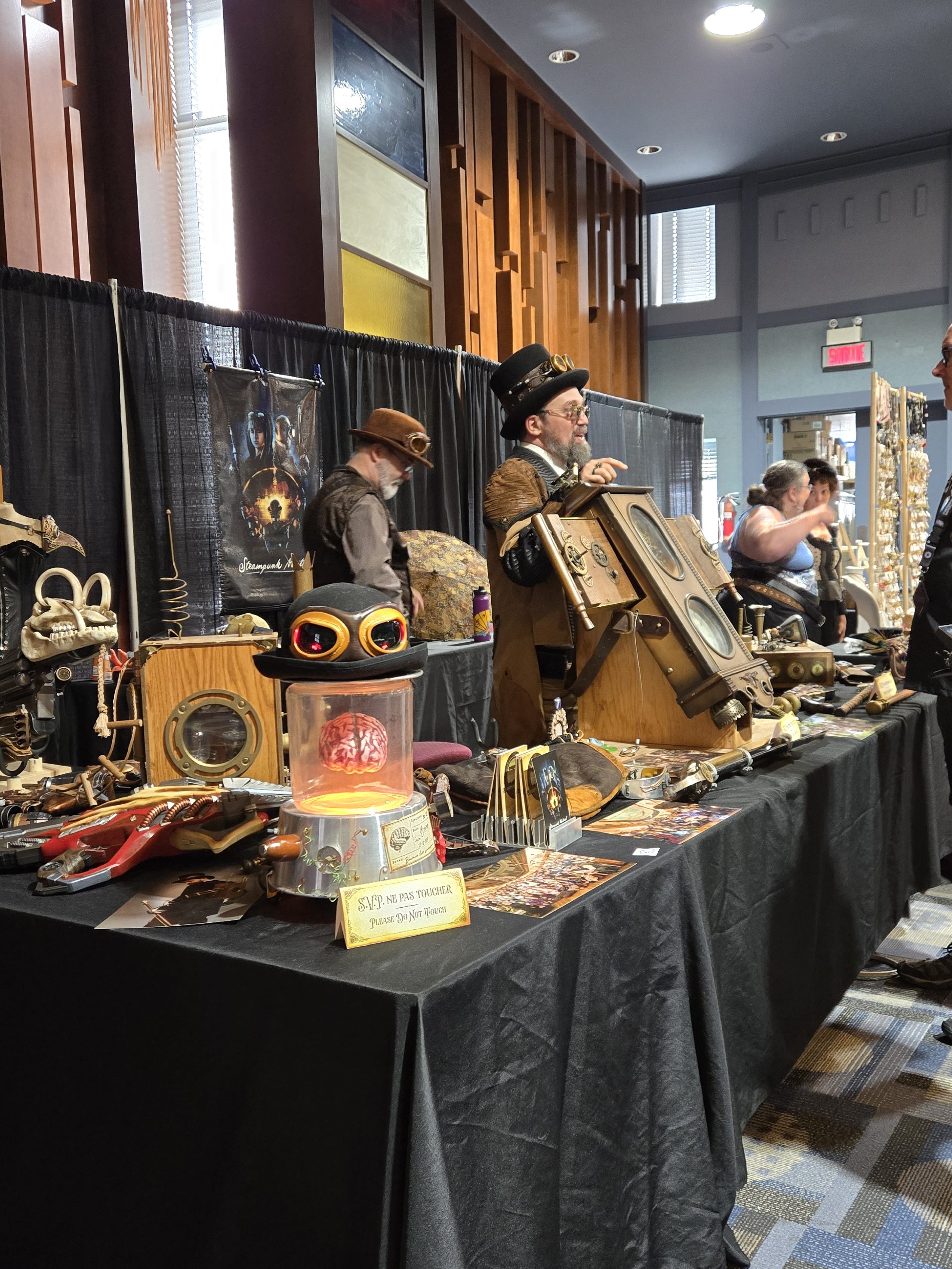 Table remplie d'accessoires victoriens ayant l'esthétique steampunk et deux personnage portant des habits victorien et des chapeaux et lunettes steampunks
