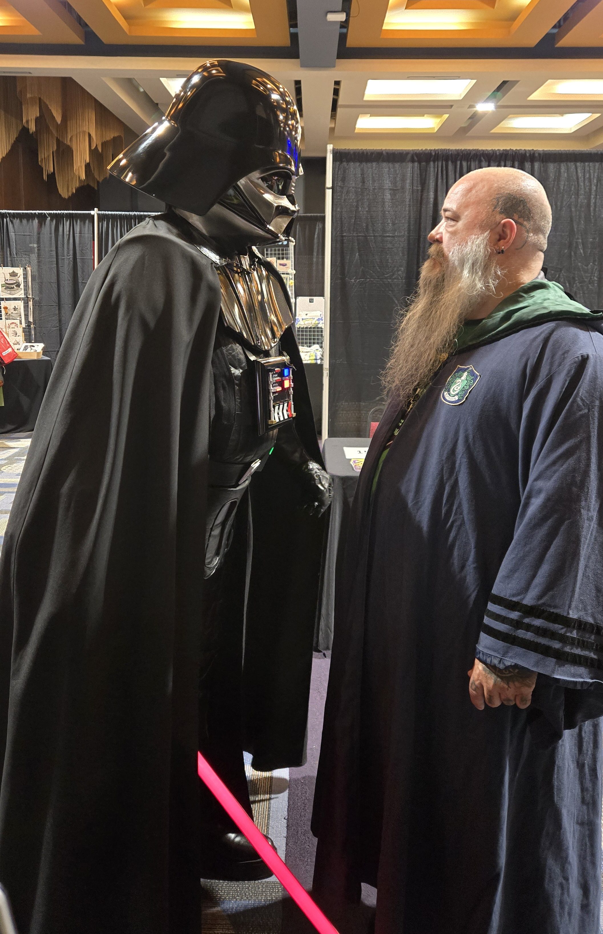 Homme costumé en Darth Vader faisant face à un homme portant une robe de Serpentard