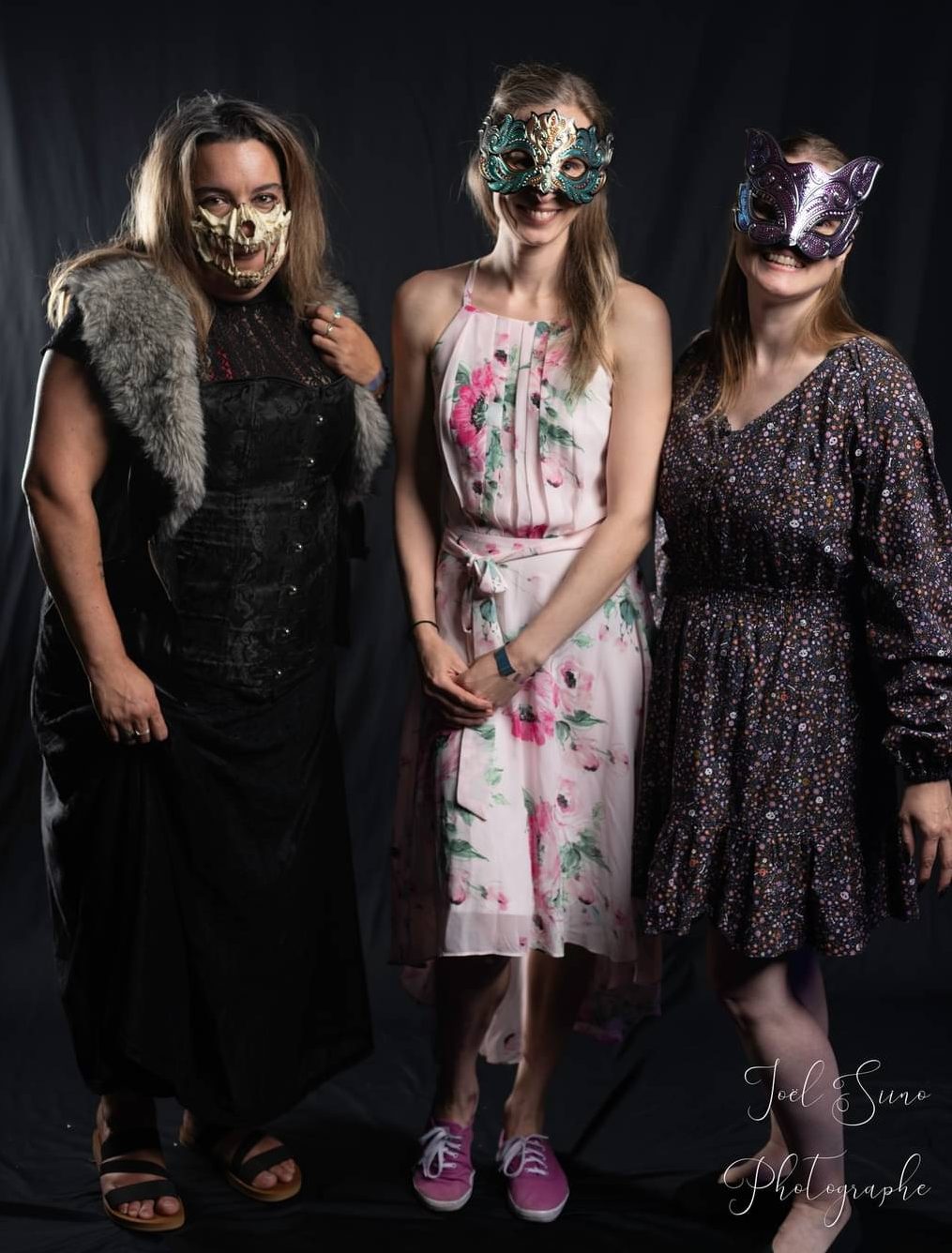 Cyntia Dubé habillée de noir et d'une veste de fourrure et portant une mâchoire d'os en guise de masque tandis que Joe et Sandrine contrastent avec leurs robes fleuries et leurs masques à paillettes.