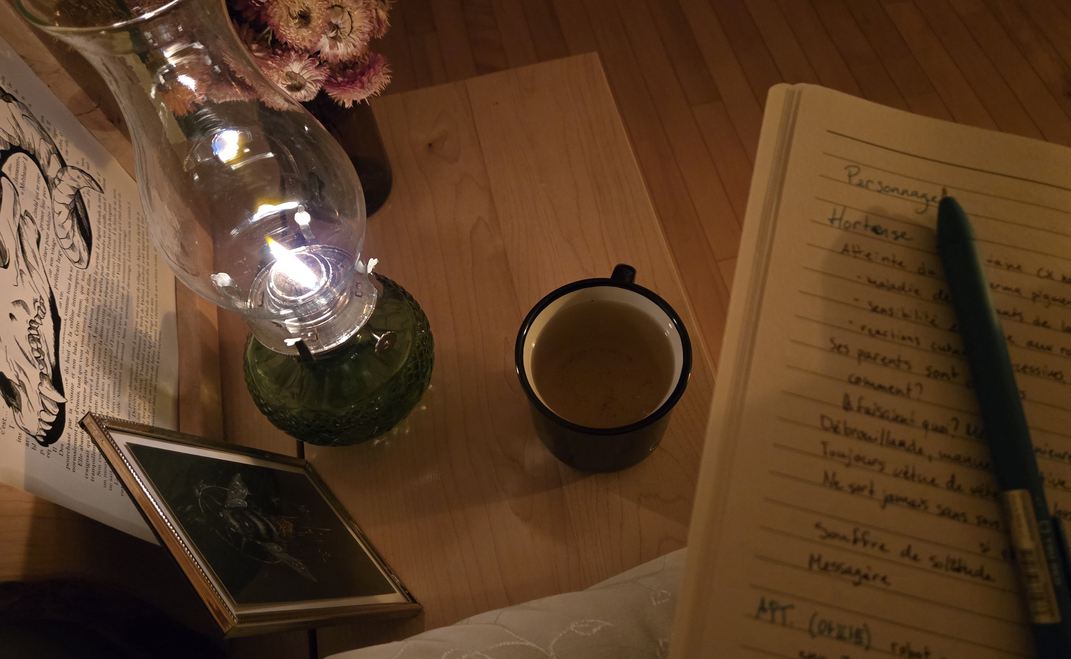 Carnet de notes avec tasse de tisane, une lampe à l'huile allumée et quelques décorations, cadres et bouquet de fleurs séchées